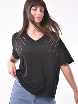 Remera negra de corte holgado con cuello en V y apliques de tachas doradas en los hombros.