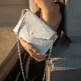 Sobre y morral en cuero blanco charol, con correa larga de cadena y cuero, y muñequera removible.