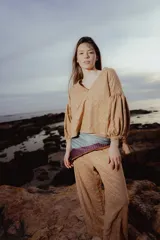 Blusa color ocre con estampado de flores, escote en V, mangas largas abullonadas con lazo en los puños y corte holgado.