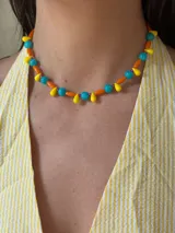 Collar corto de cuentas de colores: esferas turquesas, cilindros naranjas y mostacillas violetas, con colgantes de gota amarillos.