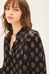 Camisa negra con estampado floral blanco, de corte regular, con volados en el cuello y cierre frontal con botones.