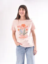 Remera color rosa claro con estampado de flores y texto en tonos naranja y azul.