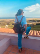 Mochila negra de cuero blando con herrajes dorados, correas marrones ajustables y cierre con cremallera.