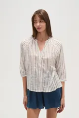 Camisa blanca de algodón con rayas verticales en tono beige/tostado y detalles de bordado tipo ojal a lo largo de las rayas. Presenta cuello mao con abertura en V y botones frontales, y mangas 3/4 con ligero volumen.