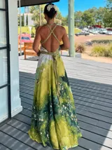 Vestido largo de tela fluida, color verde esmeralda con estampado abstracto en tonos turquesa y detalles dorados. Diseño asimétrico con un solo tirante tejido en el hombro.