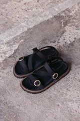 Sandalias planas color tostado con tiras cruzadas y hebillas doradas.