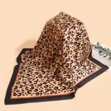 Pañuelo cuadrado de tela satinada con estampado animal print en tonos beige y negro, con borde negro y detalles en naranja.