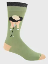 Par de calcetines de algodón con temática de golf. Un calcetín presenta un campo de golf con bandera roja y cielo azul. El otro calcetín muestra una figura inclinada golpeando una pelota de golf con un palo. El cuerpo principal es verde oliva, con puntera y talón en amarillo claro y puño superior en negro/verde oscuro.