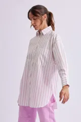 Camisa oversize blanca con rayas verticales rosas, de manga larga con puños abotonados, cuello clásico y bolsillo de parche en el pecho.