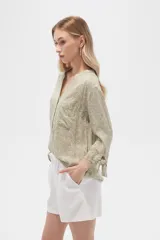 Blusa color beige con estampado de arabescos blancos, cuello mao, mangas 3/4 con lazos en los puños, cierre parcial con botones y bolsillos frontales.