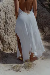 Vestido largo de color blanco, con escote en V pronunciado y tiras largas que permiten anudarlo de múltiples formas. Presenta tajo en ambos laterales y forro interno.