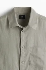 Camisa manga larga color verde oliva, de corte recto, con cuello inglés, tapeta clásica, canesú en la espalda, bolsillo superior abierto, cierre ajustable de botón en los puños y bajo redondeado.