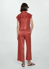 Camisa azul sin mangas de tejido fluido y satinado, con cuello camisero, cierre frontal con botones y bolsillo de parche en el pecho.