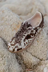 Zapatilla urbana con capellada de cuero con textura tipo pelo con estampado animal print en marrón y blanco, detalles en gamuza marrón, cordones marrones y suela de goma color caramelo.
