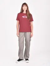 Remera blanca de manga corta con cuello redondo y un estampado artístico en tonos rojo oscuro y negro que simula una figura femenina con pantalón ancho a rayas.