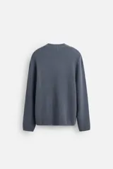 Sweater azul de punto con textura, corte holgado, cuello redondo y mangas largas con puños acanalados.
