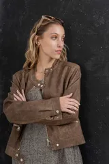 Chaqueta tipo biker de cuero ecológico (PU) color marrón con acabado desgastado, cuello Mao con broches metálicos, cierre frontal y bolsillos con cremallera.