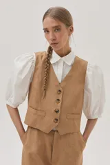 Camisa blanca de mangas abullonadas con puños elásticos, cuello clásico y cierre frontal con botones. Presenta detalles de bordado calado en el pecho.