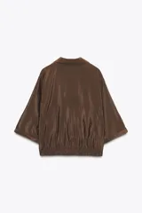 Camisa marrón de cuello solapa y manga corta con trabilla y botón. Tiene bolsillos delanteros de plastrón con solapa, bajo elástico y cierre frontal con botones a presión.