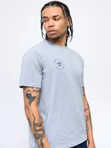 Remera color crema de corte clásico con cuello redondo y estampado en la espalda de una huella digital con forma de pelota de fútbol y el logo de Umbro.