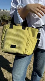 Cartera negra tipo tote bag con diseño capitoneado, doble asa corta y correa larga ajustable. Incluye bolsillos laterales y bolsillo frontal amplio.