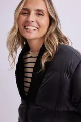Campera puffer negra con cuello en V, cierre frontal con botones a presión y puños tejidos.