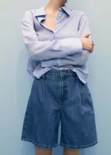 Short de jean azul de tiro medio, con pinzas delanteras, bolsillos laterales y cierre frontal con cremallera y botón.