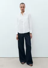 Camisa blanca de lino 100%, con diseño recto, cuello camisero, manga larga con puños abotonados y bolsillo de parche en el pecho.