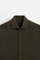 Camisa verde oscuro de corte regular, confeccionada en tejido de mezcla de algodón y lyocell. Tiene cuello italiano, manga larga con puños abotonados y cierre frontal con botones.