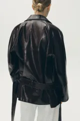 Trench corto marrón de efecto piel, con cuello solapa, manga larga con puños, bolsillos de vivo en el delantero y cinturón del mismo tejido.