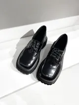 Mocasines negros de cuero vacuno con cordones, ojalillos metálicos y suela track.