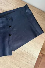 Top corto de cuero ovino color azul metalizado, con breteles finos y cierre frontal con botones a presión.