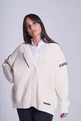 Cárdigan color beige con botones negros, escote en V y detalles de costuras bordadas en negro.