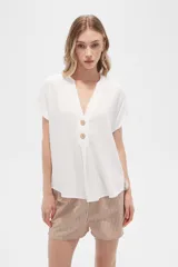 Blusa color crudo de viscosa, corte holgado, con cuello en v y cierre frontal con dos botones de madera.