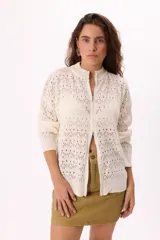 Cárdigan tejido calado color crudo con cierre frontal, cuello alto y mangas largas.