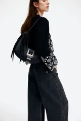 Blusa cropped de algodón color negro con bordado de flores blancas, mangas largas abullonadas, escote en V con volados y cierre frontal con lazos.