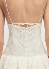 Vestido corto blanco con textura, tirantes finos y espalda abierta con lazo. Tiene escote de pico, cierre de cremallera en la parte posterior y corte globo.