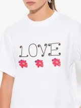 Remera blanca de algodón pima con estampado de la palabra "Love" en negro y tres flores rojas.
