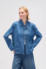 Chaqueta de jean azul con cuello camisero, cierre frontal con lazos y bolsillos de parche.