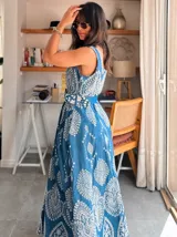 Vestido largo de jean azul con bordado floral blanco, corte evasé, sin mangas y con cinturón.