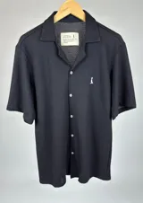 Camisa negra tejida de manga corta con cuello solapa, cierre frontal con botones blancos y logo bordado en el pecho.