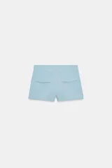 Shorts de tiro medio color negro, con bolsillos delanteros y falsos bolsillos con solapa en la parte trasera. Cierre frontal con cremallera y ganchos metálicos.