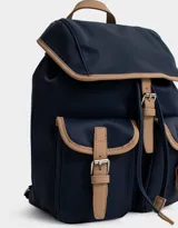 Mochila azul marino con detalles en cuero sintético color camel. Tiene solapa superior con cierre de hebilla, doble bolsillo frontal con hebilla, correa de ajuste y manija superior.