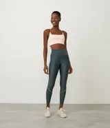 Calza deportiva larga color gris oscuro, de tiro alto y corte ajustado, con detalle de bies blanco contrastante en la parte inferior de la pierna.