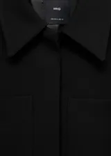 Chaqueta corta negra de corte recto con cuello camisero, manga larga, dos bolsillos de parche delanteros, cierre frontal con botones ocultos y forro interior.