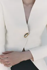 Chaqueta color crema de punto con escote en pico y manga larga. Cierre frontal con un botón dorado.