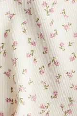Conjunto de pijama de dos piezas en punto acanalado color blanco con estampado de pequeñas flores rosas. El top es de breteles finos con ribete de encaje en el escote y bajo sobrehilado. El short tiene cintura elástica y bajo sobrehilado.