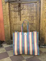 Bolso tipo tote grande con rayas verticales en celeste, blanco y bordó. Tiene doble asa corta en celeste con borde bordó, cierre superior y bolsillo interno.