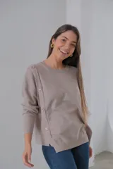 Sweater color beige de tejido de punto, corte recto y cuello redondo. Presenta detalle de botones decorativos en el hombro y lateral.