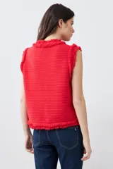 Chaleco tejido color rojo con cuello redondo, sin mangas, con desflecado en bordes y bolsillos frontales con botones dorados.